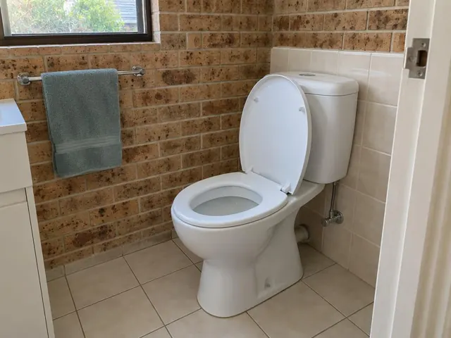 Clean white toilet in a tiled bathroom with brick wall and towel rail in St Ives