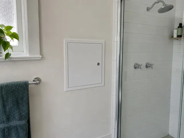 Bathroom wall with a small access panel beside a tiled shower in Gordon
